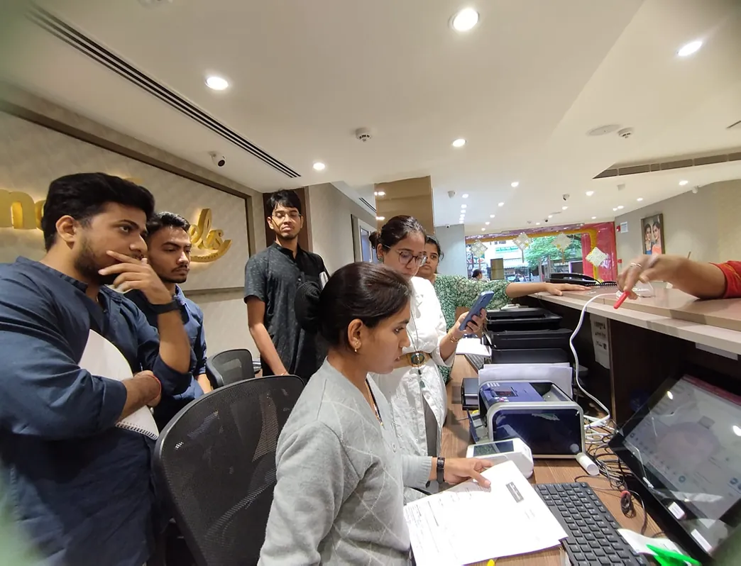 The team standing at a Reliance Jewels store counter, watching a sales assistant work through an enrolment.